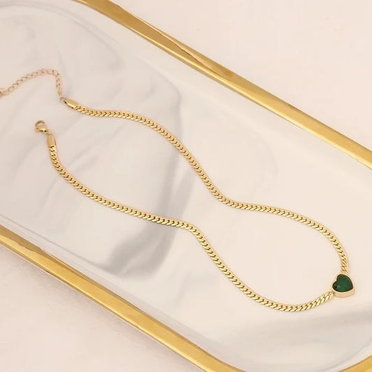 Χρυσό κολιέ με πράσινη καρδιά από ζιργκόν τοποθετημένο σε λευκό δίσκο.