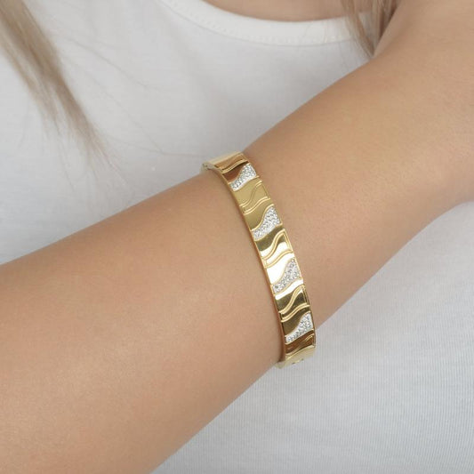 Χρυσό βραχιόλι με κυματιστά μοτίβα και λαμπερά ζιργκόν για μοντέρνα κομψότητα.