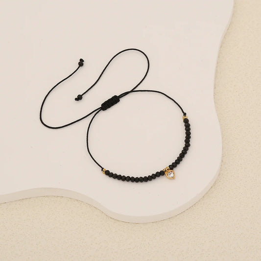 Μαύρο βραχιόλι με πετραδάκια και χρυσή καρδιά με κρύσταλλο.